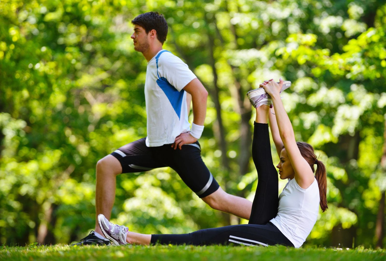 Frauen, die Yoga auf grünem Gras in der Nähe von Bäumen ausüben